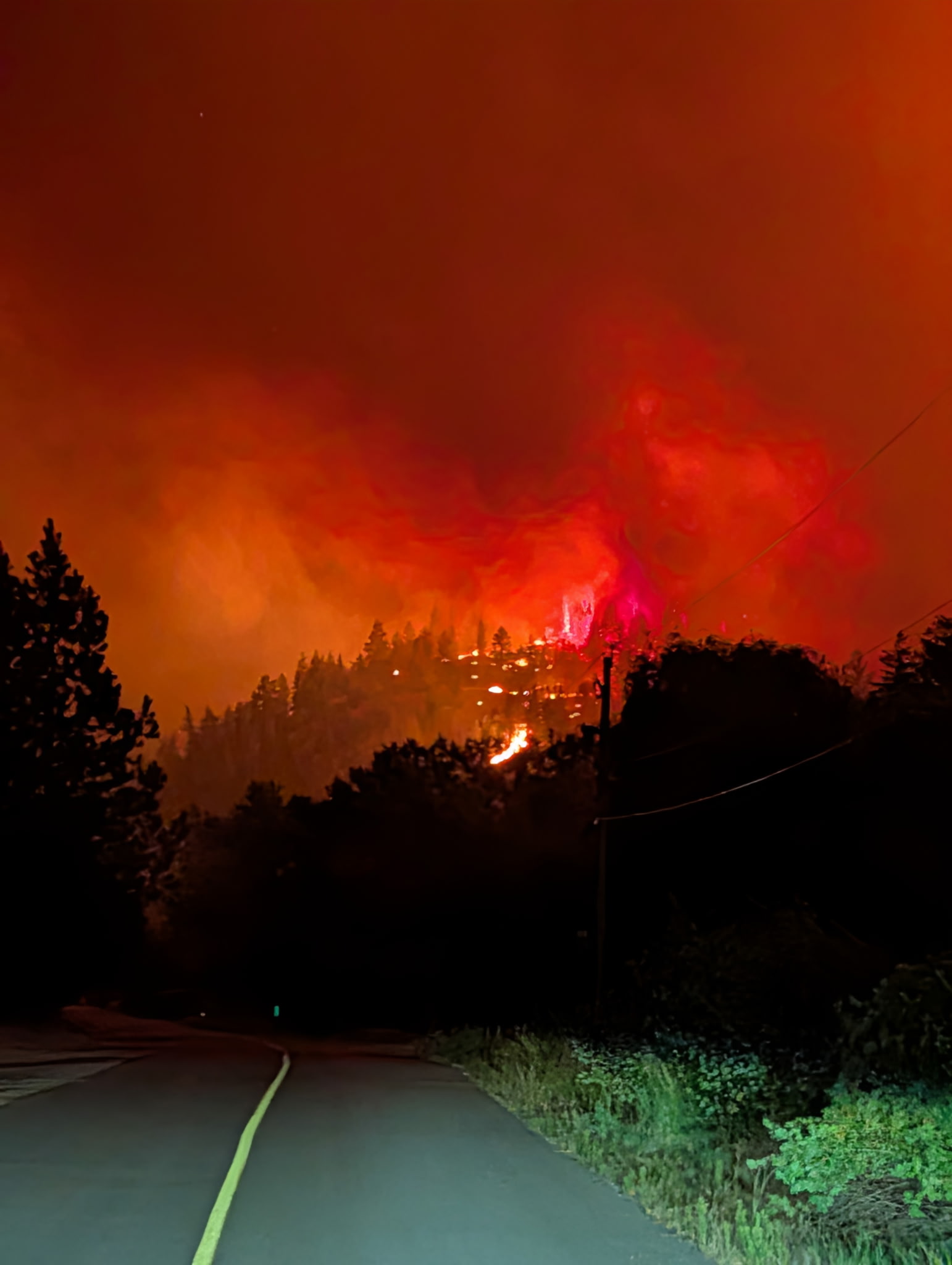 A rural road at night beneath a ridge glowing red with active fire.